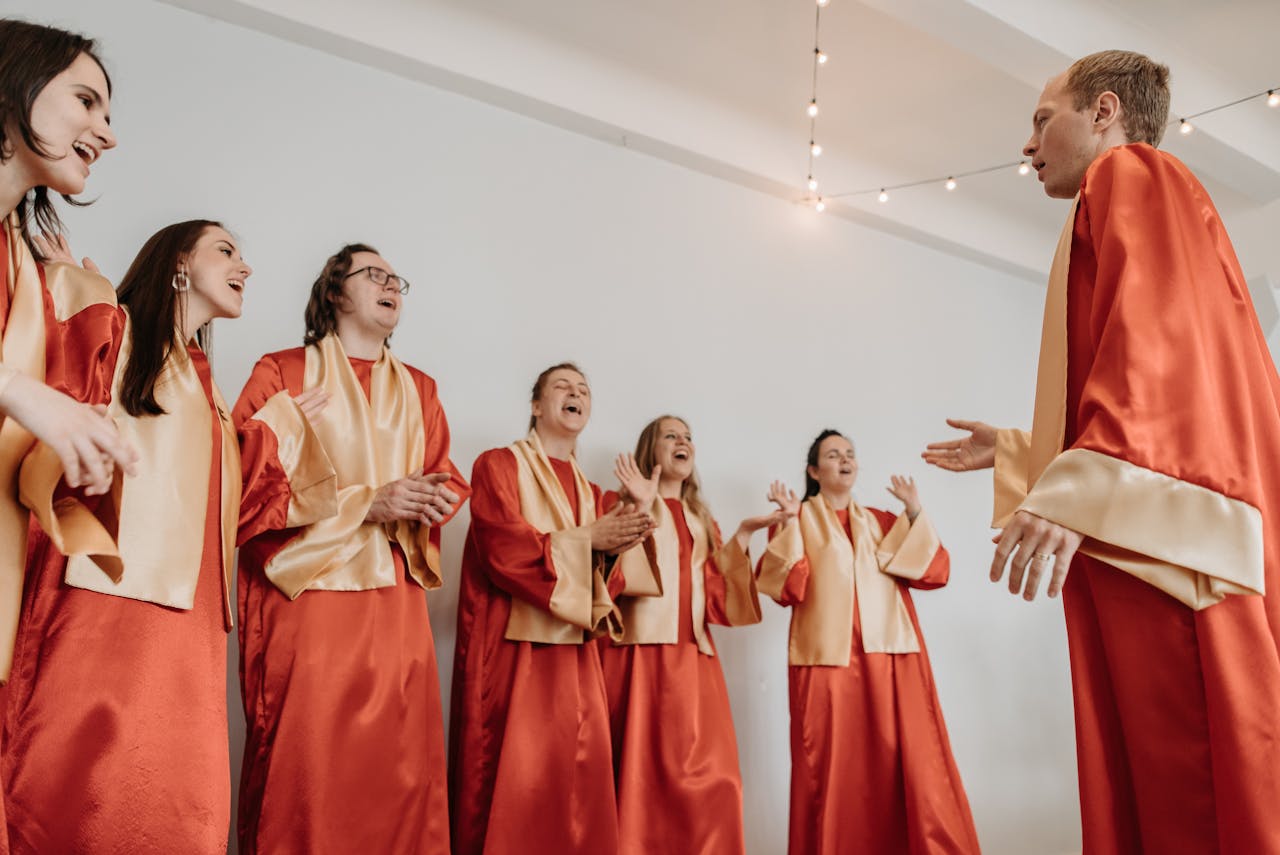 A diverse choir group joyfully sings in red and gold robes in an indoor setting.